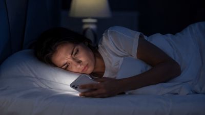 Женщина ночью лежит в кровати и с недоумением смотрит на экран телефона, получив сообщение от мужчины